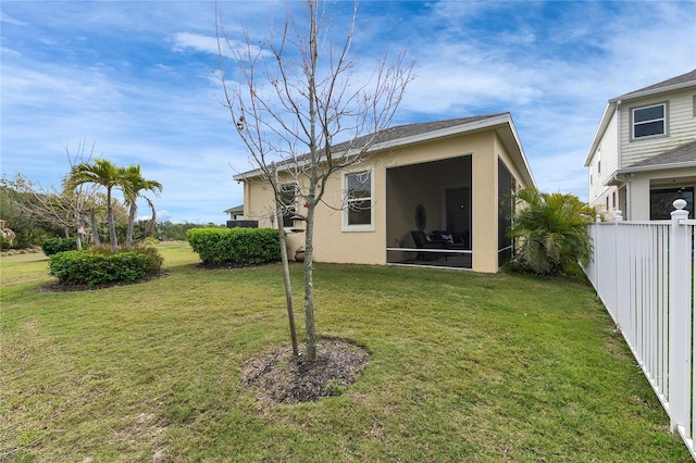 rear view of property featuring a lawn, fence, a sunroom, and stucco siding