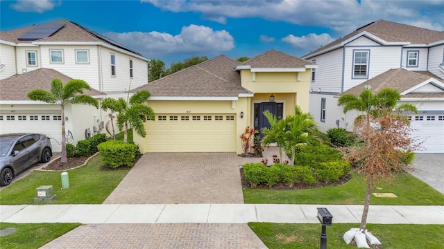 traditional-style house with a garage, a shingled roof, decorative driveway, and stucco siding