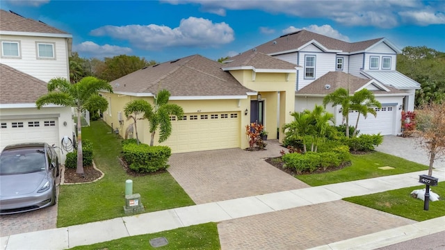 traditional-style house with a shingled roof, decorative driveway, an attached garage, and a front lawn