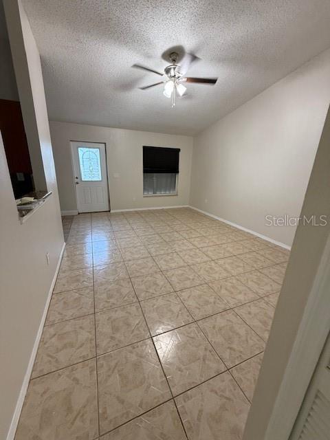 interior space with a textured ceiling, light tile patterned flooring, a ceiling fan, and baseboards