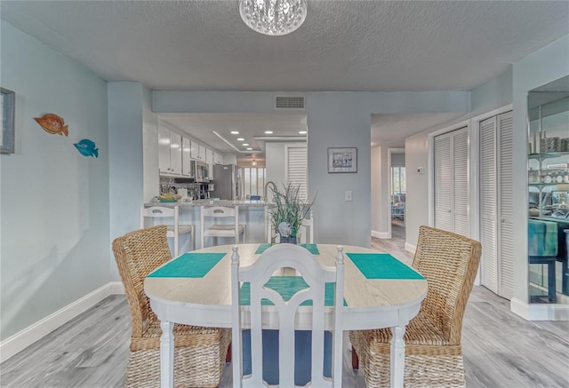 dining room featuring visible vents, light wood-style flooring, a textured ceiling, and baseboards