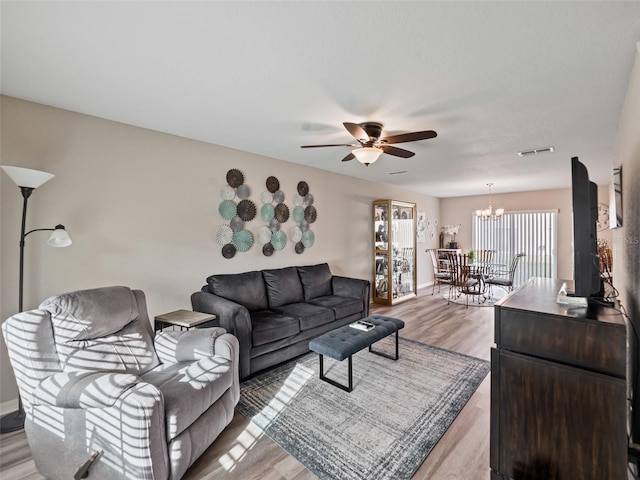 living area featuring light wood-type flooring, visible vents, baseboards, and ceiling fan with notable chandelier