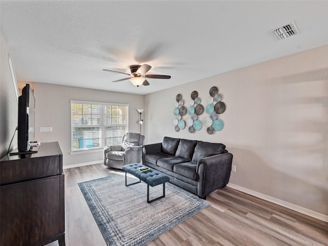 living area with visible vents, ceiling fan, baseboards, and wood finished floors