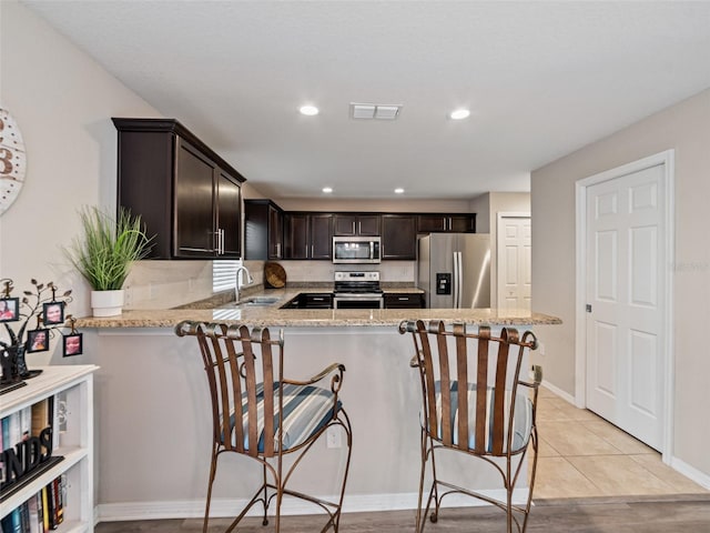 kitchen featuring dark brown cabinets, appliances with stainless steel finishes, a sink, and light stone countertops