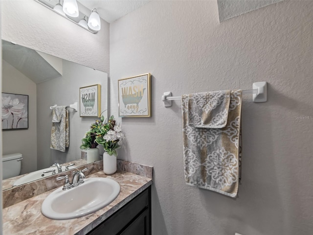 bathroom with a textured wall, vanity, and toilet