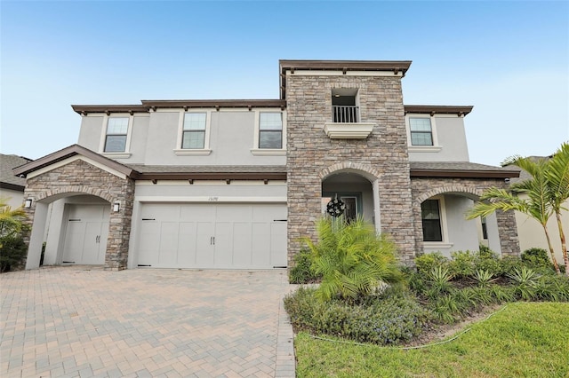 view of front facade featuring stone siding, decorative driveway, an attached garage, and stucco siding