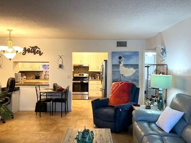 living area featuring light tile patterned floors, a textured ceiling, visible vents, and a notable chandelier