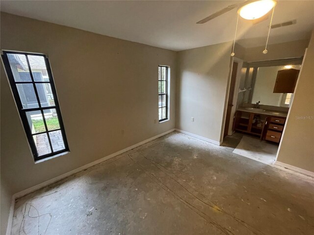 empty room featuring a ceiling fan, visible vents, a sink, and baseboards