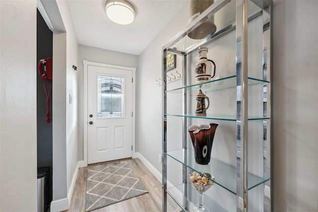 doorway to outside with a textured ceiling, baseboards, and wood finished floors