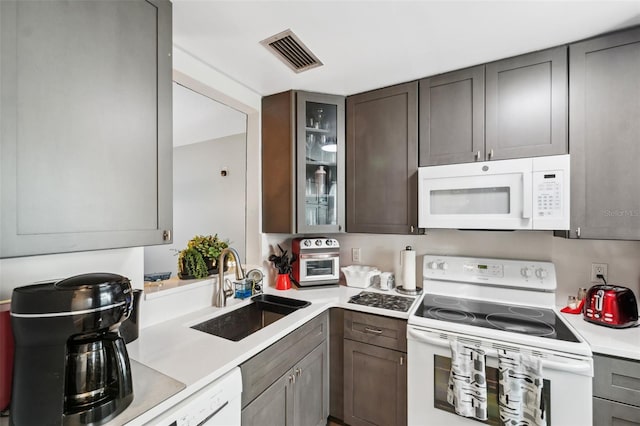 kitchen featuring white appliances, a sink, visible vents, light countertops, and glass insert cabinets