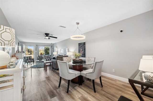 dining room featuring a ceiling fan, visible vents, baseboards, and wood finished floors