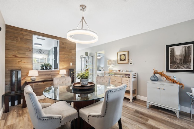 dining space featuring light wood-type flooring, wooden walls, and baseboards