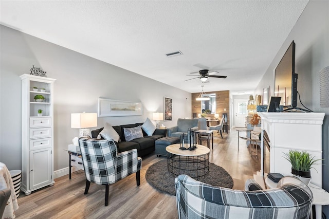 living area featuring a textured ceiling, a ceiling fan, visible vents, and light wood-style floors