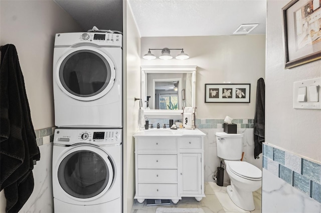 washroom featuring laundry area, visible vents, a wainscoted wall, stacked washing maching and dryer, and tile walls