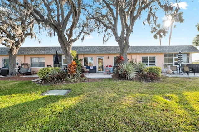 rear view of property featuring a shingled roof, a patio area, a lawn, and stucco siding