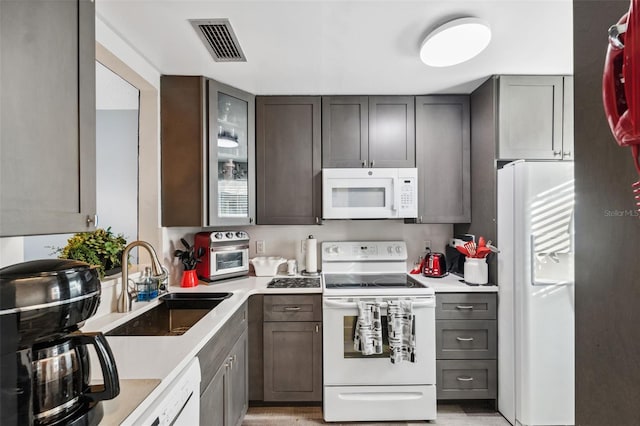 kitchen with white appliances, visible vents, glass insert cabinets, light countertops, and a sink