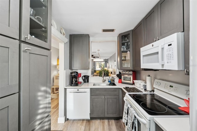 kitchen with white appliances, a sink, visible vents, light wood-type flooring, and glass insert cabinets