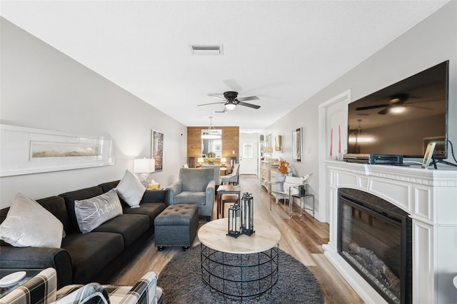 living room with a glass covered fireplace, visible vents, ceiling fan, and light wood finished floors