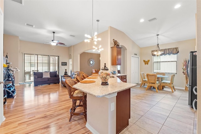 kitchen featuring visible vents, arched walkways, a kitchen breakfast bar, a peninsula, and vaulted ceiling