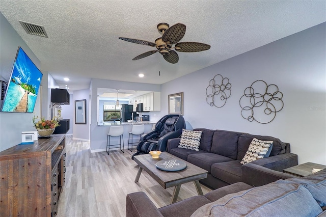 living room with light wood finished floors, visible vents, baseboards, ceiling fan, and a textured ceiling