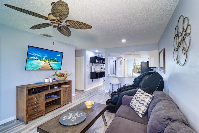 living room with a textured ceiling, ceiling fan, visible vents, baseboards, and light wood finished floors