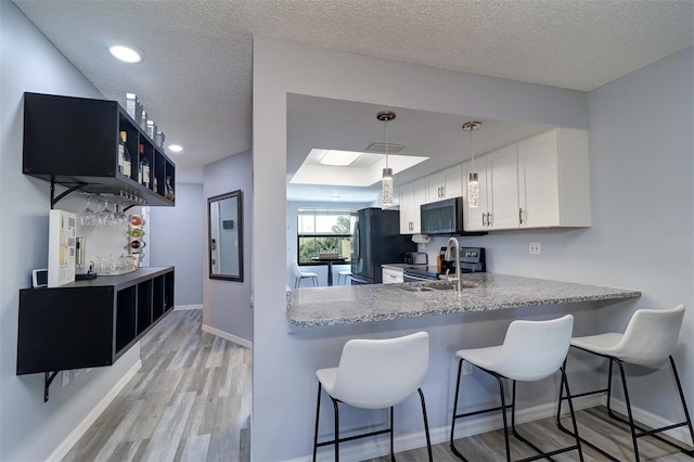 kitchen featuring a textured ceiling, light stone counters, light wood-style floors, white cabinets, and black appliances