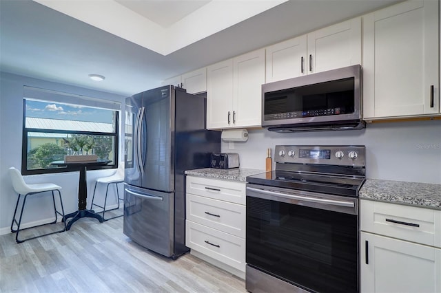 kitchen with appliances with stainless steel finishes, light wood-style flooring, white cabinetry, and light stone countertops