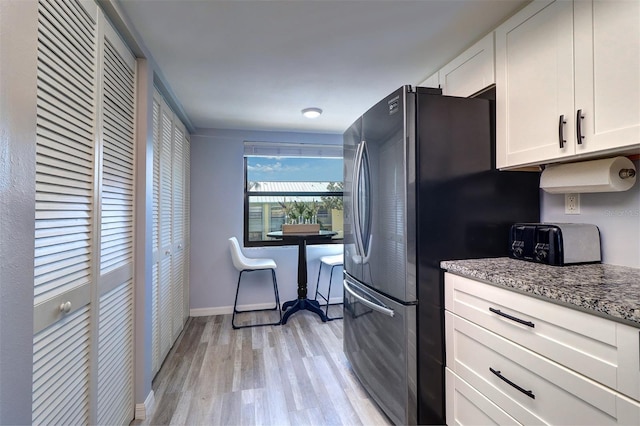 kitchen with baseboards, white cabinets, light stone counters, freestanding refrigerator, and light wood-type flooring