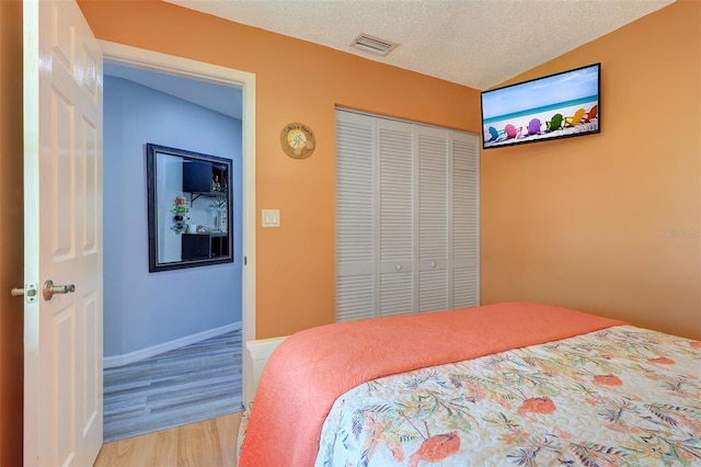 bedroom with a closet, visible vents, light wood-style floors, a textured ceiling, and baseboards