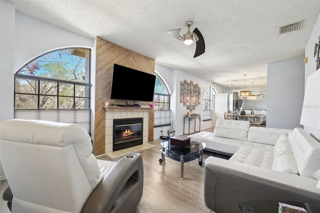 living area with visible vents, a tile fireplace, wood finished floors, a textured ceiling, and a ceiling fan