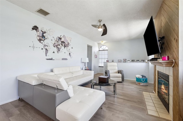 living room with visible vents, a ceiling fan, a tiled fireplace, a textured ceiling, and wood finished floors