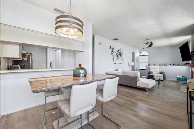 dining room with visible vents, baseboards, a textured ceiling, and wood finished floors