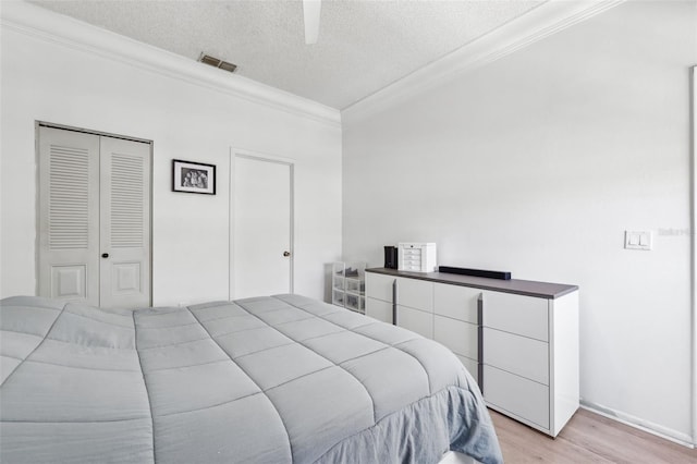 bedroom with visible vents, ornamental molding, light wood-style floors, a textured ceiling, and a ceiling fan