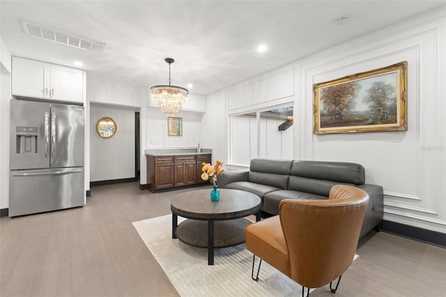 living room featuring light wood-type flooring, an inviting chandelier, and visible vents