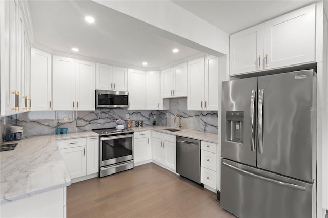 kitchen with white cabinets, wood finished floors, a sink, stainless steel appliances, and backsplash