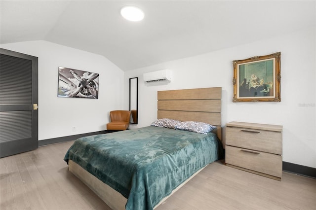 bedroom with vaulted ceiling, an AC wall unit, baseboards, and light wood-style floors