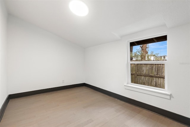 empty room with baseboards, vaulted ceiling, and wood finished floors