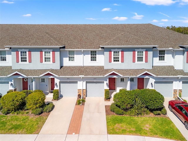 multi unit property with stone siding, roof with shingles, driveway, and stucco siding