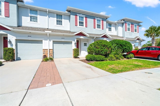 multi unit property with a garage, stone siding, driveway, and stucco siding