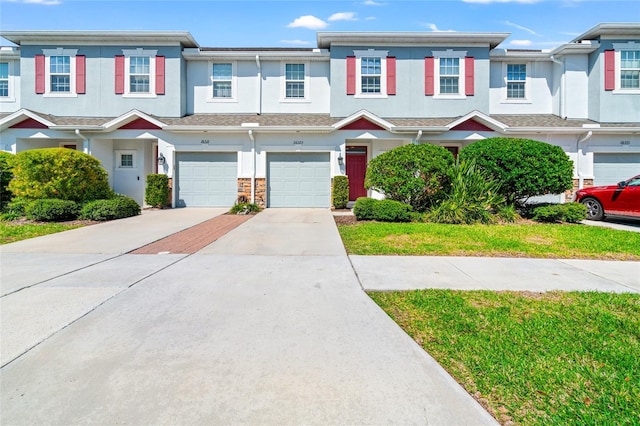 townhome / multi-family property with a garage, driveway, stone siding, and stucco siding