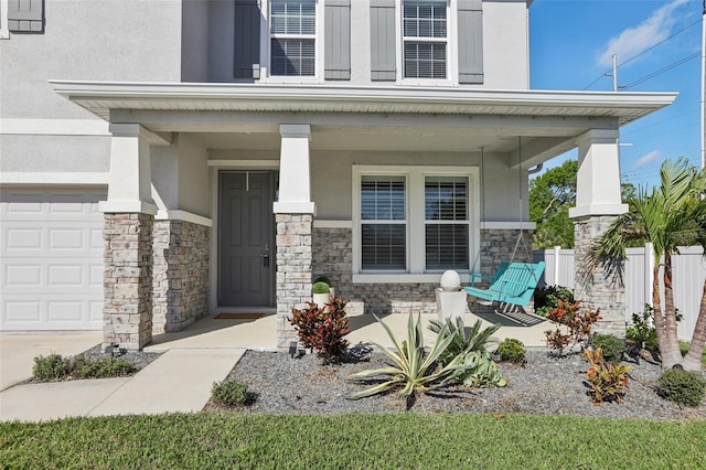 property entrance with fence, covered porch, stone siding, and stucco siding