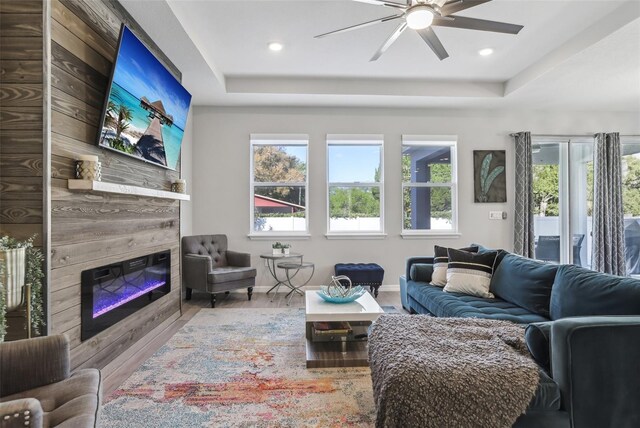 living room featuring a raised ceiling, wood finished floors, a fireplace, and ceiling fan