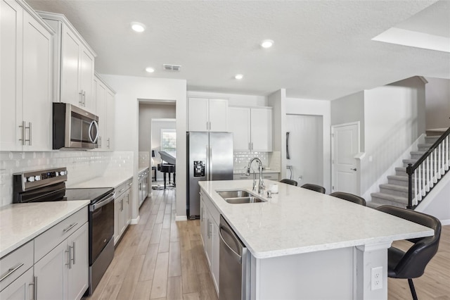 kitchen featuring visible vents, a sink, appliances with stainless steel finishes, a kitchen bar, and light wood-type flooring