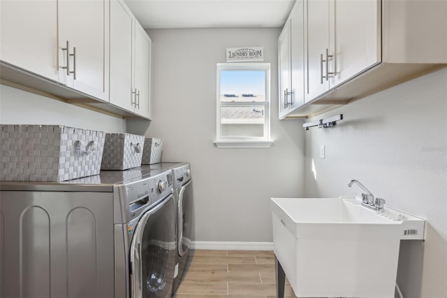 clothes washing area with washing machine and clothes dryer, baseboards, wood finish floors, cabinet space, and a sink