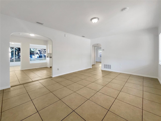 spare room featuring arched walkways, visible vents, baseboards, and light tile patterned floors