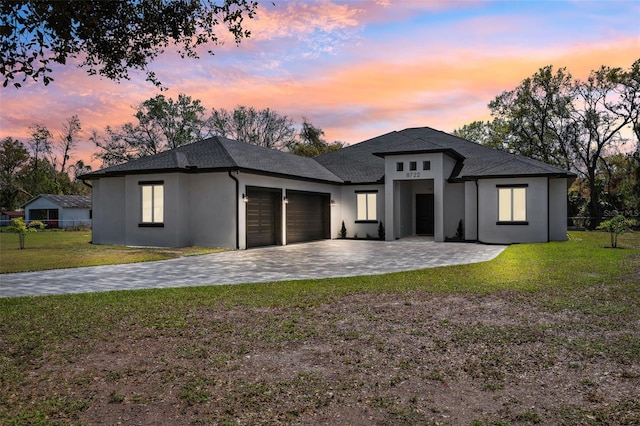 view of front facade with a garage, stucco siding, decorative driveway, and a yard