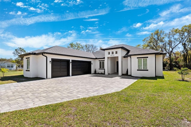 prairie-style house featuring a garage, decorative driveway, a front lawn, and stucco siding