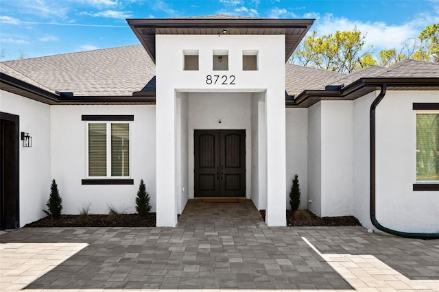 doorway to property featuring stucco siding and roof with shingles