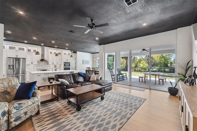 living room featuring a textured ceiling, light wood-type flooring, and visible vents