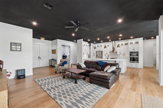 living area featuring light wood-style floors, visible vents, and a ceiling fan